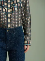 Camisa de viscosa con estampado a cuadros de estilo retro en tonos beige, azul marino, celeste y rojo. Presenta cuello camisero, cierre frontal con botones metálicos plateados y diseño con capas superpuestas en el pecho de inspiración country.