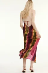 Vestido midi de cuello halter y escote en V, con diseño tie-dye en tonos fucsia, borgoña y verde. Presenta un nudo decorativo en el delantero, espalda descubierta y abertura frontal en el bajo.