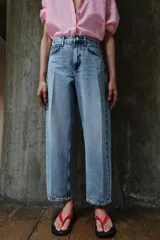 Pantalón de jean tiro medio con diseño barrel, caracterizado por su pernera holgada que se estrecha hacia el tobillo. Presenta cinco bolsillos, cierre frontal con cremallera y botón, y detalle de raya planchada en el frente.