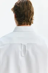 Camisa Oxford de algodón blanca, de corte regular fit, con cuello americano, bolsillo frontal aplicado y mangas largas con puños abotonados.