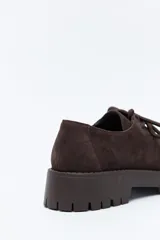 Zapato de gamuza color marrón con cordones, puntera con costura marcada y suela robusta dentada.
