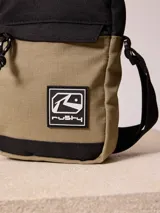 Bandolera negra de poliéster con logo de la marca Rusty en relieve en el frente. Cuenta con un bolsillo frontal con solapa y cierre de cremallera en el compartimento principal. La correa es ajustable.