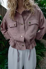 Chaqueta corta marrón de cuello solapa y manga remangada por debajo del codo. Presenta bolsillos delanteros de plastrón con solapa, bajo ajustable con cordón interior y cierre frontal con botones.