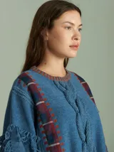 Sweater oversize de lana con diseño de trenza central, detalles en tejido cuadrillé y terminaciones desflecadas. Presenta mangas acampanadas, cuello a la base y aberturas laterales con tiras ajustables.