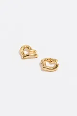 Caravanas de aro con forma de corazón y acabado metálico plateado. Presentan un diseño de líneas fluidas y cierre de gancho. Fabricadas en latón.