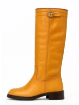 Bota alta de cuero color ocre con caña recta, puntera redondeada y hebilla decorativa en la parte superior.
