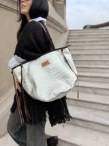 Cartera tipo tote bag de color plateado con textura de reptil, marca Antonia. Cuenta con correas de hombro y detalles de tiras laterales en color marrón oscuro, además de un parche con el logo de la marca en el frente.
