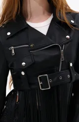 Campera corta estilo biker confeccionada en cuero sintético, con cierre frontal asimétrico, solapas anchas y cinturón ajustable en la cintura. Presenta un diseño distintivo con flecos largos que caen desde el dobladillo, aportando movimiento y un estilo bohemio.