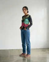 Remera de manga larga con estampa abstracta y orgánica que combina tonos verde, turquesa, magenta, azul y tierra sobre base negra. Presenta cuello redondo y silueta ajustada.