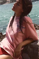 Camiseta oversize de manga corta y cuello redondo, color rosado con efecto lavado, con pequeño texto estampado en azul en el pecho.