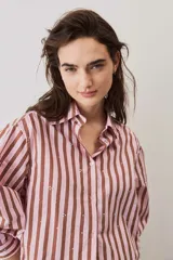 Camisa a rayas verticales en tonos rosado y marrón, de manga larga abullonada, cuello camisero y cierre frontal de botones con pequeños apliques brillantes.