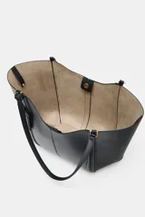 Bolso tipo shopper de hombro en color beige, con diseño estructurado, doble asa y detalle de pespuntes verticales en el cuerpo. Incluye un colgante decorativo tipo etiqueta y cierre imantado.