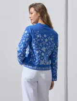 Chaqueta de algodón bordada, color azul con bordado floral blanco, con cuello a la base y escote en V, abertura central con botón.