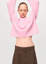 Jersey de punto trenzado color rosado, con cuello redondo y mangas largas de corte recto.