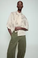 Camisa de corte holgado confeccionada en mezcla de lyocell, con estampado de rayas verticales en tonos neutros y azules. Presenta cuello redondo con lazada frontal, cierre con botones ocultos y mangas amplias por debajo del codo.