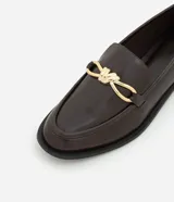Zapato mocasín femenino de PU color negro, con punta cuadrada y detalle metálico dorado en el empeine. Tiene un tacón bajo y suela de goma.