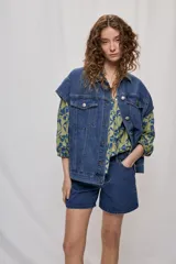 Chaleco oversize de jean negro, con cuello camisero, cierre frontal con botones metálicos y bolsillos delanteros.