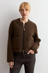 Chaqueta reversible de corte recto con cierre frontal de cremallera. Presenta un lado en acabado de gamuza negra y el reverso en tejido de textura tipo corderito color marrón chocolate, con cuello redondo y bolsillos frontales.