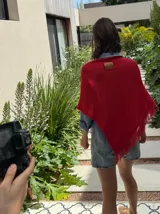 Poncho tejido en hilo de algodón, color rojo, con diseño de cuello redondo y terminaciones con flecos en el ruedo.