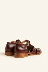 Sandalia cerrada tipo pescador de cuero negro charol, con tira en T y hebilla ajustable en el tobillo. Posee suela y taco bajo de madera.