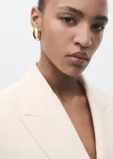 Chaqueta de traje color beige, con cuello de solapa, cierre cruzado con un botón y bolsillos con solapa en los laterales y en el pecho.