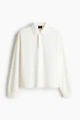 Remera polo de manga larga confeccionada en punto suave de algodón, con cuello inglés de sarga y tapeta con botones ocultos. Presenta hombros caídos, puños acanalados y aberturas laterales en el bajo, con un corte holgado.