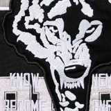Campera con capucha y cierre frontal completo, confeccionada en algodón negro. Presenta múltiples aplicaciones gráficas bordadas y estampadas en el frente, mangas y capucha, con motivos deportivos y tipografía estilo varsity.