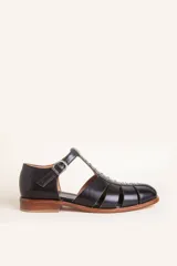 Sandalia de cuero negro estilo romana, con tiras anchas, taco bajo de madera y detalle de tachas metálicas en la tira central. Cuenta con cierre de hebilla lateral.