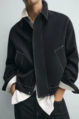 Sobrecamisa de corte regular fit color negro con pespuntes en contraste blancos. Presenta cuello solapa, mangas largas con puños abotonados, bolsillos frontales de vivo y cierre de cremallera oculta por solapa con botones.