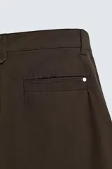 Pantalón chino de corte wide fit confeccionado en tejido de algodón. Presenta pliegues frontales, bolsillos laterales y bolsillos traseros de vivo, con cierre frontal de cremallera y botón.