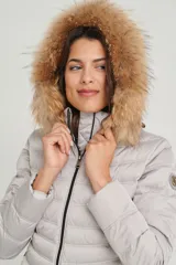 Campera puffer color beige con relleno de plumón, cierre central con cremallera de doble carro, bolsillos laterales y capucha desmontable con borde de piel sintética marrón. Largo 70cm.