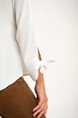 Camisa blanca de manga larga con cuello mao y cierre frontal con botones. Las mangas tienen nudos decorativos en los puños.