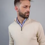 Buzo de punto color beige con cuello alto y medio cierre frontal.