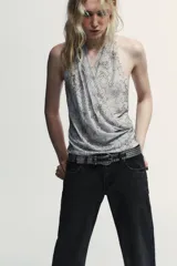 Top halter de tul color gris claro, con escote fluido drapeado y espalda descubierta. Presenta bordados con aplicación de abalorios en tonos oscuros y dorados.