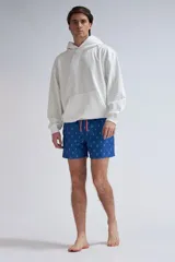 Short de baño para hombre, color azul vibrante, con estampado repetitivo de arabescos en blanco. Presenta cordón de ajuste naranja en la cintura.