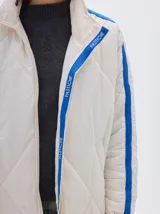 Campera marrón claro con diseño acolchado de rombos, cuello alto, cierre frontal con cremallera, bolsillos laterales y mangas largas con rayas blancas.