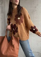 Sweater de punto grueso color camel, con diseño de flores grandes aplicadas en tonos marrones y centro crema. Presenta cuello redondo alto, mangas largas con hombros caídos y terminaciones acanaladas.