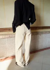 Jeans de tiro alto color beige con diseño recto, cinco bolsillos y detalles bordados calados en la parte inferior de las piernas.