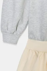 Vestido corto que combina una parte superior tipo sudadera gris de manga larga con puños, y una falda corta de volantes color crema. La parte superior es de tejido de punto jaspeado y la falda tiene dos capas de volantes.