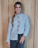 Camisa de manga larga con estampado de rayas verticales en tonos crudo y beige. Presenta cuello alto con volados, cierre frontal con botones dobles y puños con volados.