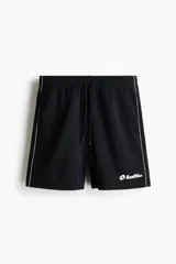 Short de futbol negro de malla, con cintura elástica y cordón ajustable. Cuenta con ribetes blancos en los laterales, bolsillos y el logo de Lotto estampado en blanco en la pierna izquierda.