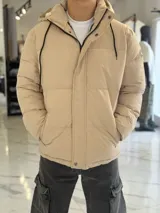 Campera puffer impermeable color beige con capucha desmontable con cordones negros, cierre frontal con cremallera y solapa con botones a presión.