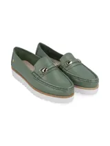 Mocasín de cuero color verde esmeralda con suela dentada blanca y detalle de hebilla metálica en el empeine.
