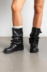 Botas de caña media confeccionadas en cuero color marrón oscuro, con diseño arrugado y dos correas con hebillas metálicas ajustables. Presentan suela plana de goma negra con un pequeño taco cuadrado.