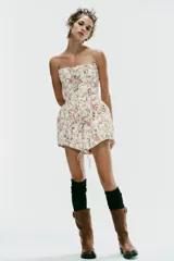 Vestido corto strapless de corte corsetero, con estampado floral en tonos rosados y verdes sobre fondo blanco. Presenta detalles de tiras cruzadas ajustables en el delantero con lazada y varillas interiores.