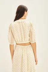 Camisa corta tipo crop top de viscosa con destellos de lurex dorado. Presenta escote en V cruzado con volados, mangas al codo con frunces en los hombros y puños elastizados.