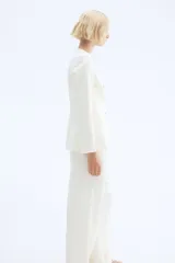 Blazer entallado color blanco roto, con cuello redondo, sin solapas, manga larga y botones frontales de madera. Posee bolsillos de parche delanteros y forro interior.