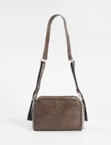 Bandolera negra de cuero vegano con correa ajustable y cadena lateral removible. Presenta un bolsillo frontal con doble cierre horizontal y un logo metálico cuadrado en la parte superior central.