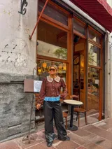 Camisa de color marrón con cuello Peter Pan en tono beige con borde de encaje, mangas largas abullonadas con puños elásticos y detalle de volado en el ruedo en color celeste.