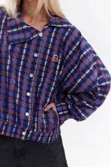 Chaqueta bomber de algodón con estampado a cuadros en tonos azules, amarillos y marrones, cuello alto y cierre frontal descentrado con botones. Cuenta con mangas abullonadas y puños elásticos.